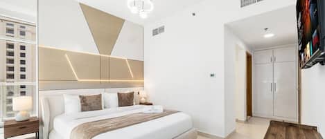 A modern hotel room with a large bed, a bedside table, a TV, and a wardrobe.