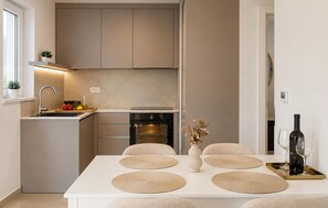 A modern kitchen with a built-in oven, a dining table with placemats, and a wine bottle on a tray. - Luxurious apartment in Kozino with WiFi (Kozino)