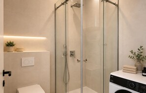 Ein modernes Badezimmer mit einer Duschkabine, einer Toilette, einer Waschmaschine und einem Ablagefach für Pflegeprodukte.
