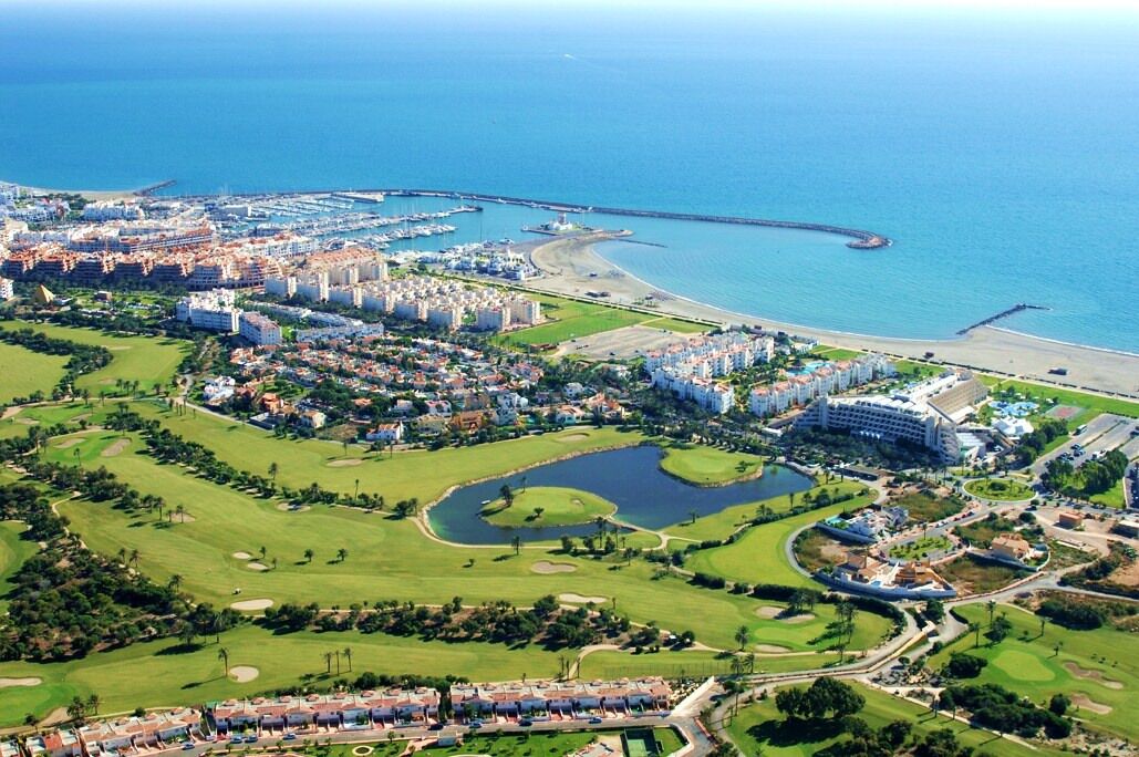 An aerial view of a coastal resort with a golf course, beachfront, and a large hotel.