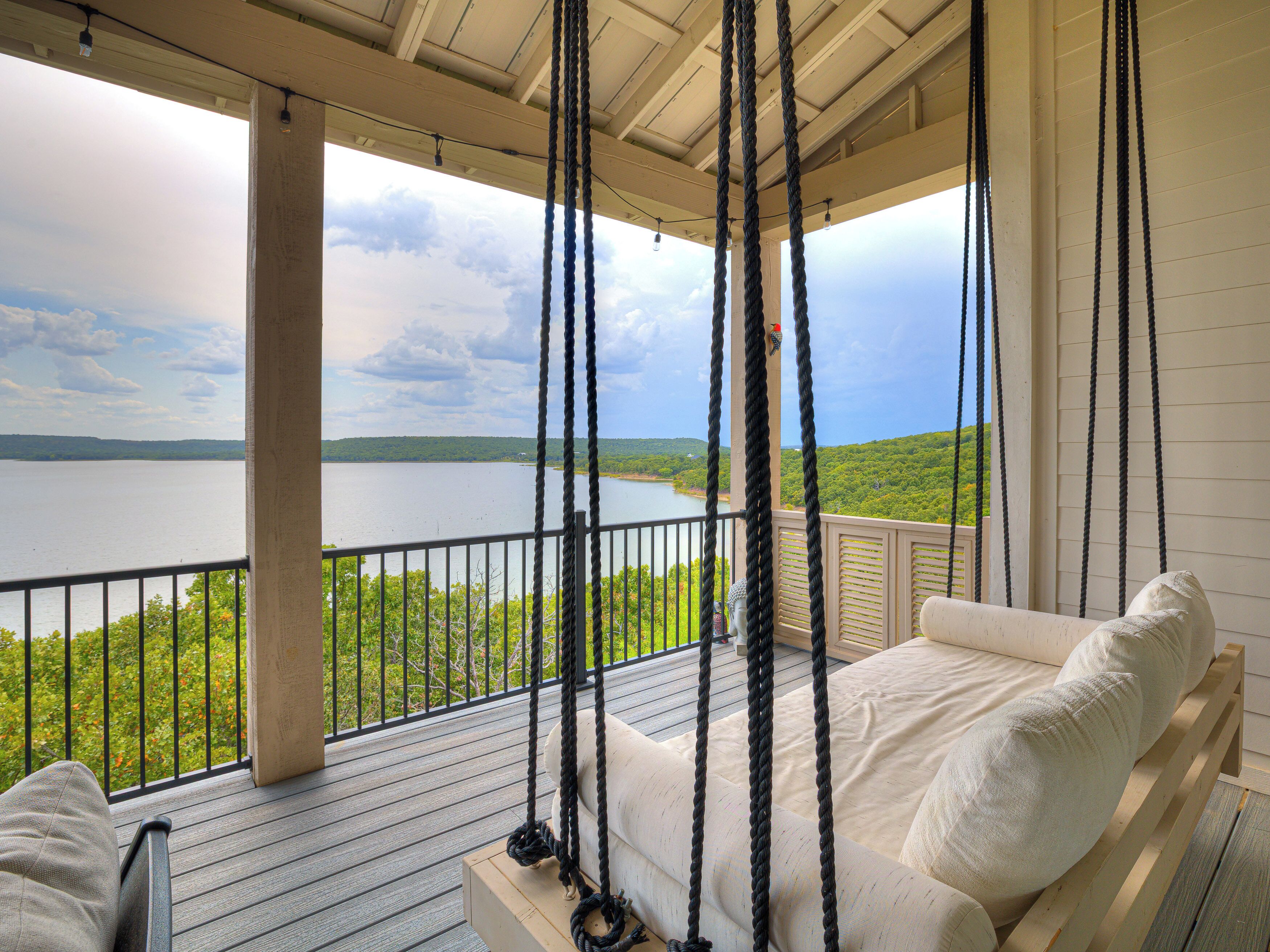 A porch with a swing chair overlooking a lake, wooden deck, and a view of the landscape.