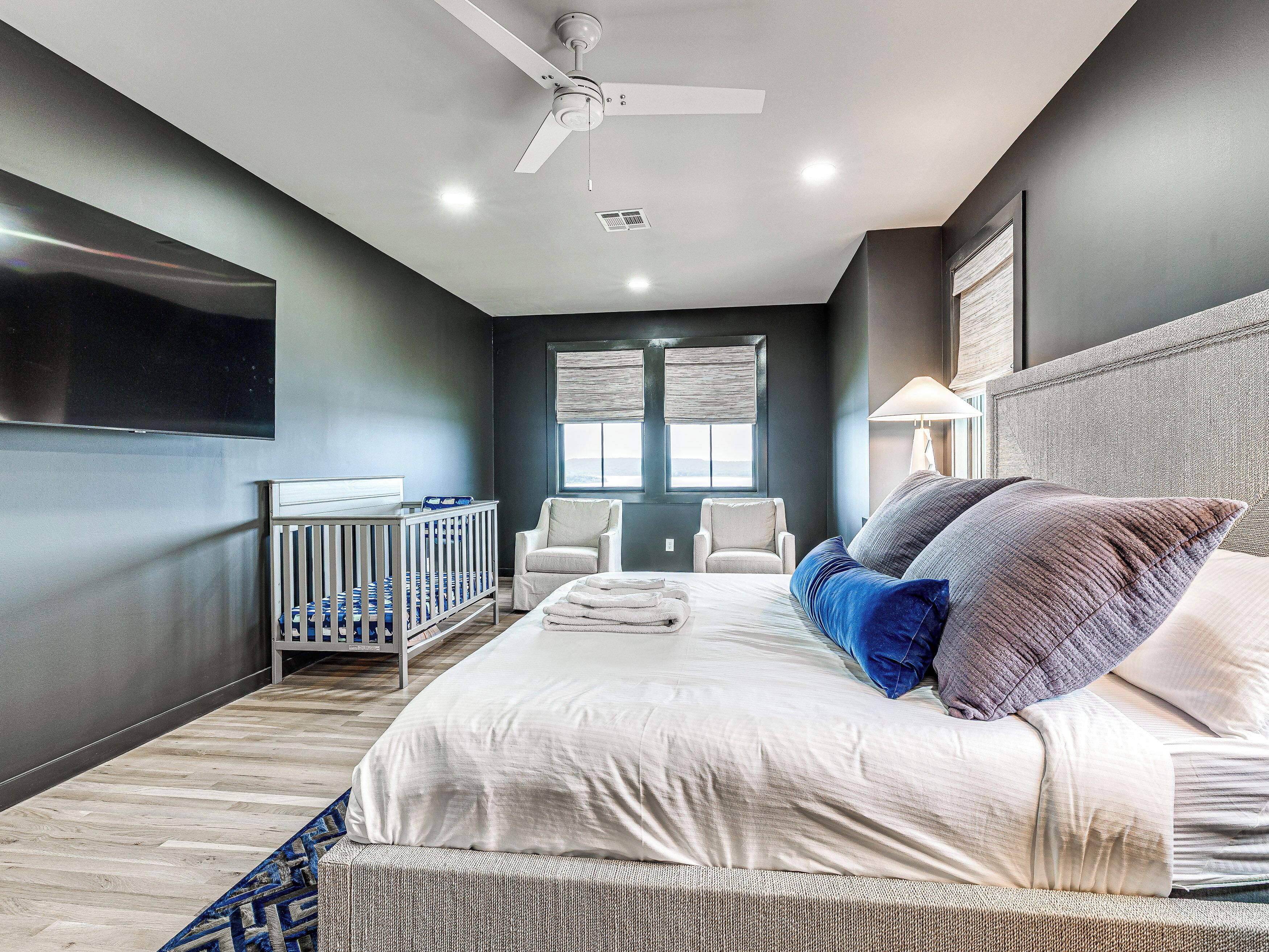 Una camera da letto moderna con un letto, una culla, un ventilatore a soffitto e una finestra con persiane.