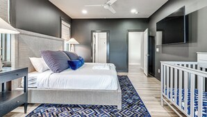 Un dormitorio moderno con cama, mesita de noche, lámpara y televisor montado en la pared.