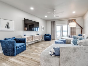 A modern living room with a flat-screen TV, a ceiling fan, and a large window with curtains. - Carlton Landing-Panorama (Carlton Landing)