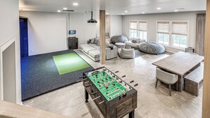 Amplia sala de estar con mesa de futbolín, un conjunto de sofás y un gran ventanal que proporciona luz natural.