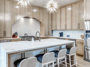 A modern kitchen with a large island, wooden cabinets, a brick backsplash, and stainless steel appliances. - Carlton Landing-Panorama (Carlton Landing)