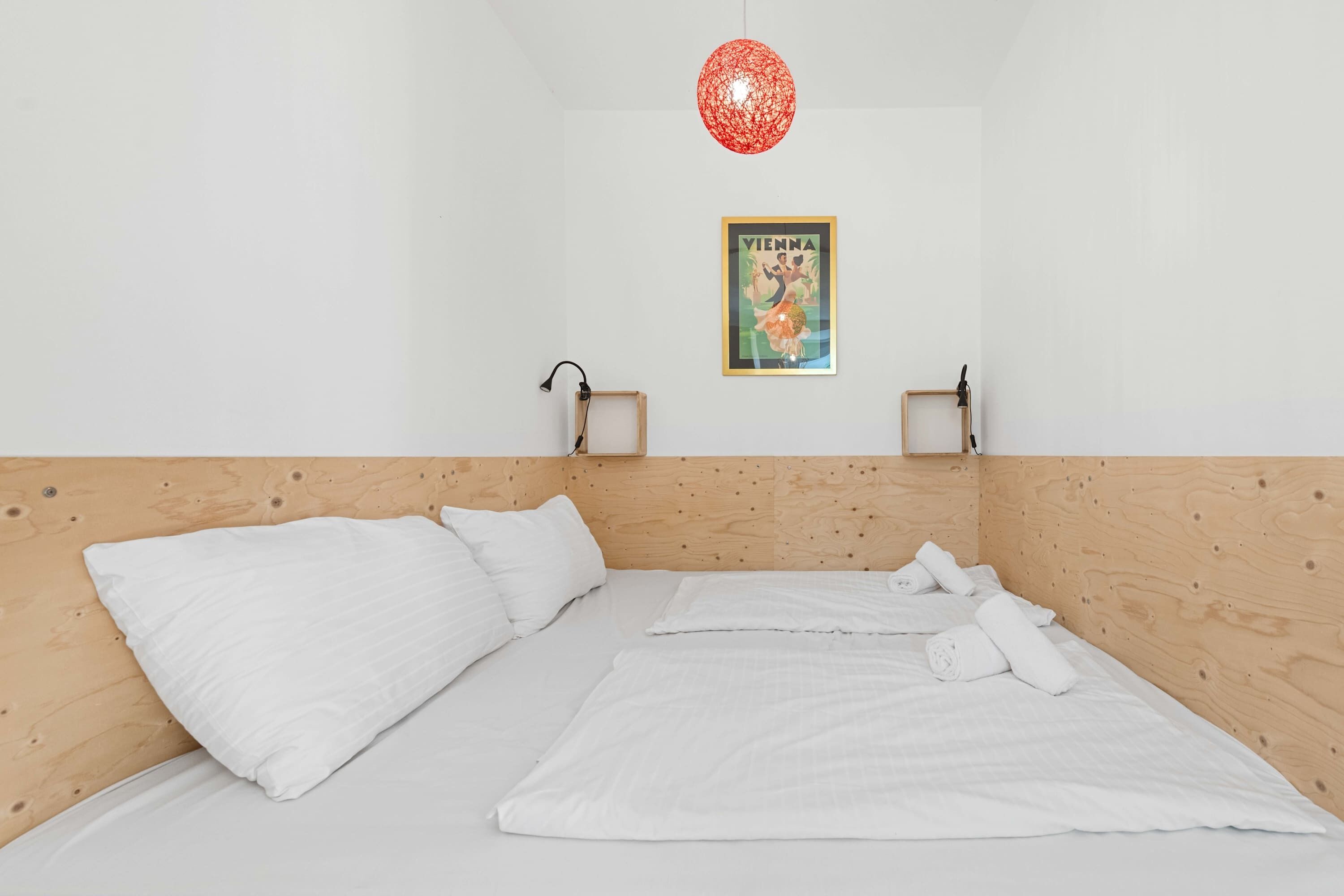 A bedroom with a wooden headboard, a bed with white linens, two wall-mounted lamps, and a framed poster on the wall.