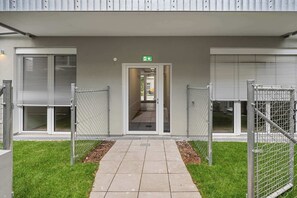 A building entrance with a pathway leading to a door marked with an emergency exit sign. - AufLeeben Vienna | Kitchen | Garage | Balcony (Wien)