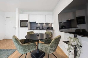 Una cocina moderna con armarios blancos, encimera negra y una zona de comedor con una mesa redonda y cuatro sillas.