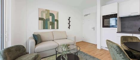 Una sala de estar moderna con un sofá, dos sillones, una mesa de centro de vidrio y una zona de cocina con microondas.
