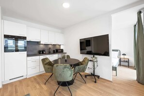 A modern kitchen with white cabinets, a built-in oven, and a microwave. There is a dining area with a round table and four chairs. - AufLeeben Vienna | Kitchen | Garage | Balcony (Wien)