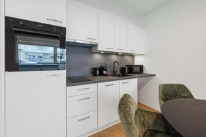 Una cocina moderna con armarios blancos, horno integrado y ventana con vista a un edificio.