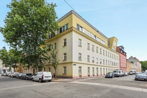 Un edifici de diversos pisos amb façana groga, cotxes aparcats i un arbre a la vorera.