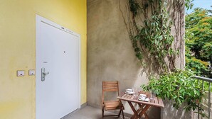 Un balcón con mesa y silla de madera, una puerta blanca y una pared cubierta de plantas trepadoras.
