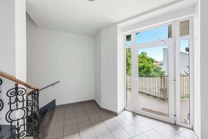 Habitació amb terra de rajola, escala de fusta amb barana metàl·lica ornamentada i una gran porta corredissa de vidre que dona a un balcó exterior.