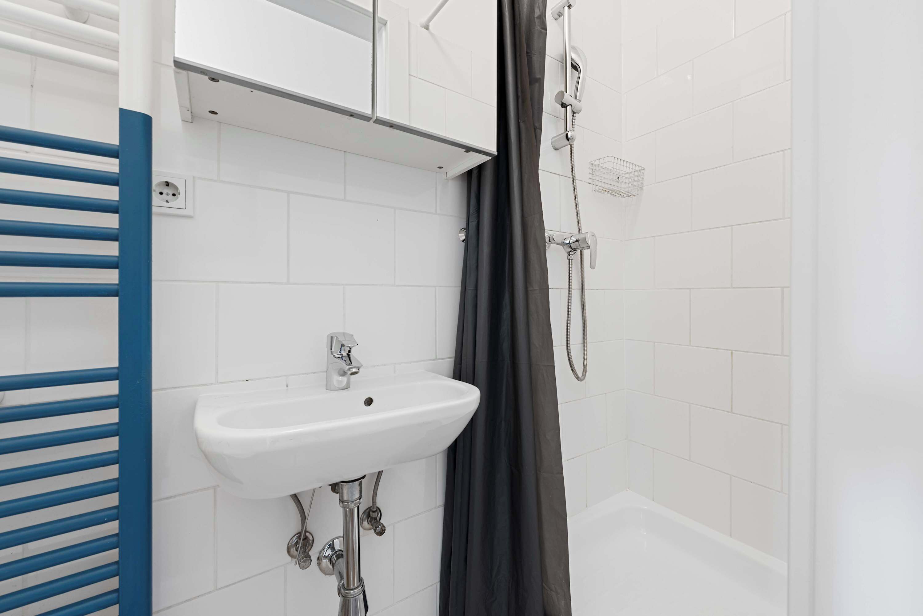 Ein Badezimmer mit einem weißen Waschbecken, einer Dusche und einem blauen Handtuchhalter.
