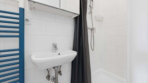 Un baño con un lavamanos blanco, una ducha y un toallero azul.