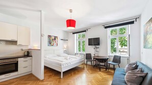 Una habitación moderna y luminosa con cama, un comedor con mesa y sillas, una cocina con estufa y un televisor montado en la pared.