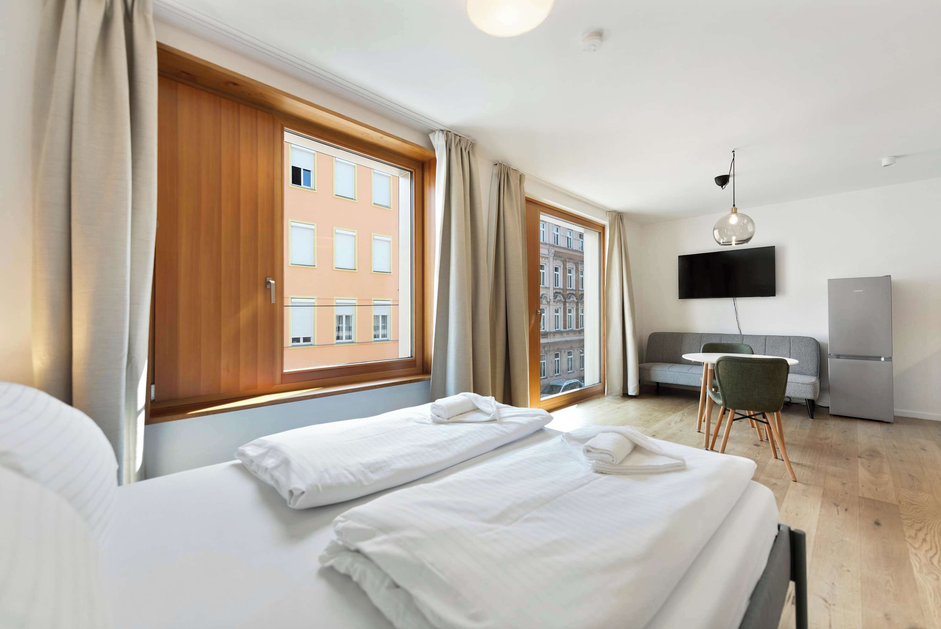 Ein Hotelzimmer mit Bett, Schreibtisch, Sessel, Fernseher und Blick auf die Stadt.