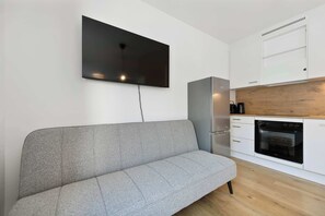 A modern kitchen with a built-in oven, a grey sofa, and a flat-screen TV mounted on the wall. - Modern Studio | King-Size | Kitchen | Metro (Wien)
