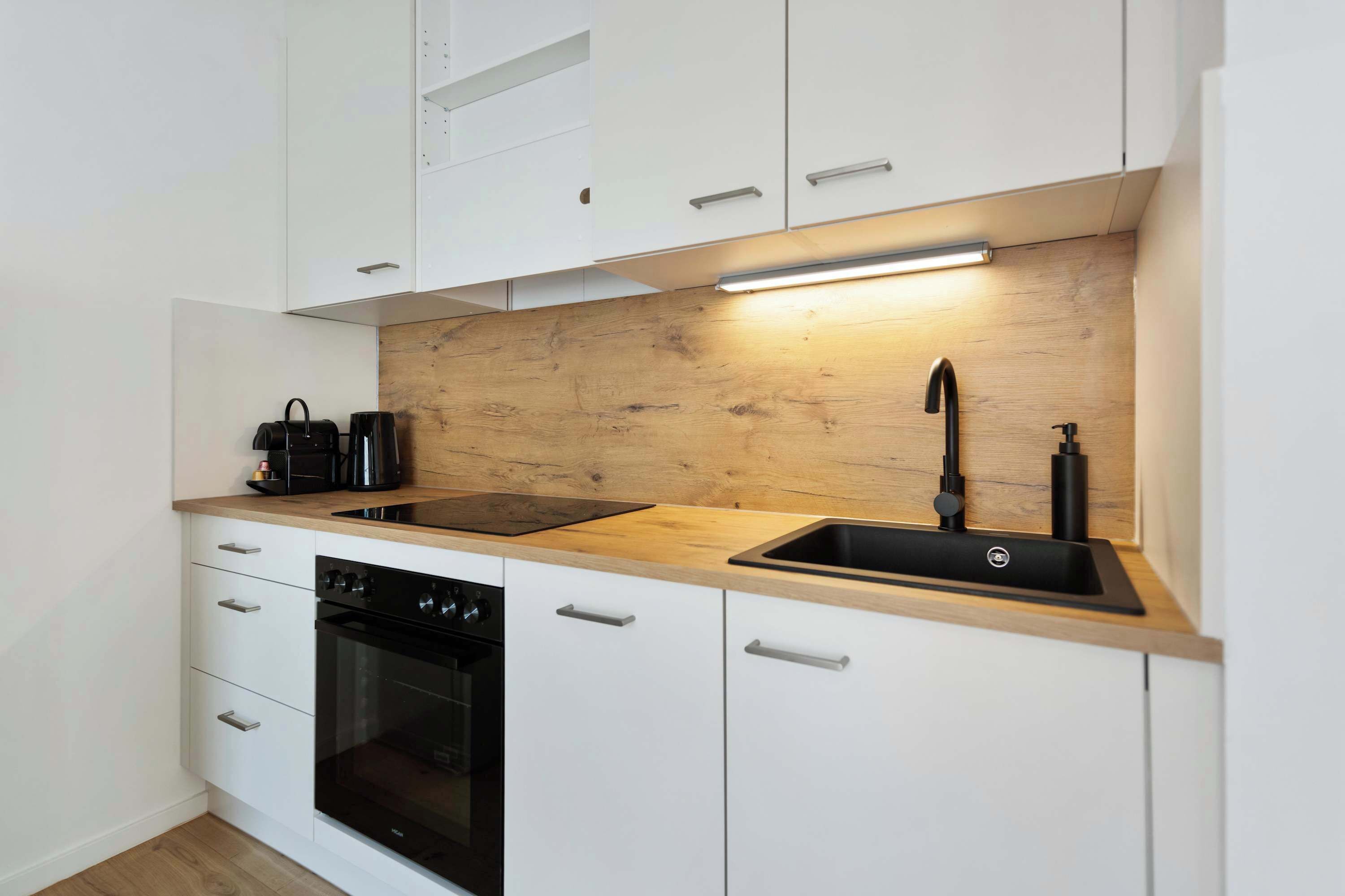 A modern kitchen with white cabinets, a wooden countertop, a built-in oven, a black stovetop, and a black sink with a faucet.