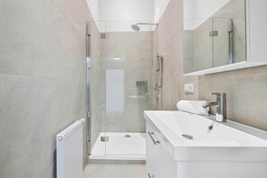 Un bagno moderno con doccia vetrata, lavandino bianco e specchio sopra il mobile.
