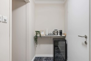 A compact kitchen with a built-in refrigerator, a coffee maker, and a small shelf with a potted plant. - Kaiser 2BR | Metro & Tram | Nespresso | Central (Wien)