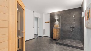 Un bany modern amb una porta de sauna de fusta, una dutxa amb mànega i un penjador de tovalloles fixat a la paret.