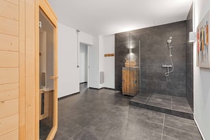 Un baño moderno con puerta de sauna de madera, ducha con cabezal de mano y toallero de pared.