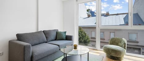 Una sala de estar moderna con un sofá gris, una mesa de centro de vidrio y un sillón verde.