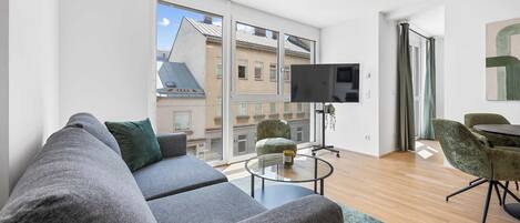 A modern living room with a grey sofa, a small round coffee table, and a TV mounted on the wall.