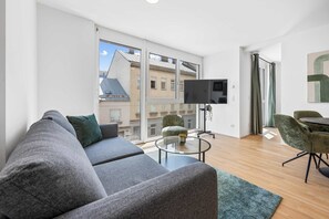 A modern living room with a grey sofa, a small round coffee table, and a TV mounted on the wall. - AufLeeben Vienna | Kitchen | King-Size | Metro (Wien)