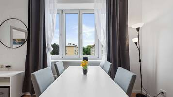 A modern room with a white dining table, grey chairs, a vase with yellow flowers, a round mirror, and a floor lamp.