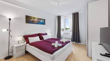 A modern bedroom with a large bed, bedside tables, a floor lamp, a painting, and a view of the outdoors through a window.