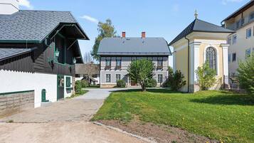 A traditional European-style building with a sloped roof, a stone foundation, and a small garden area with grass and flowers.
