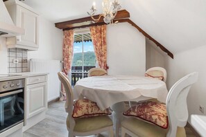 Une cuisine avec des meubles blancs, un fourneau et une fenêtre ornée de rideaux à motifs floraux.