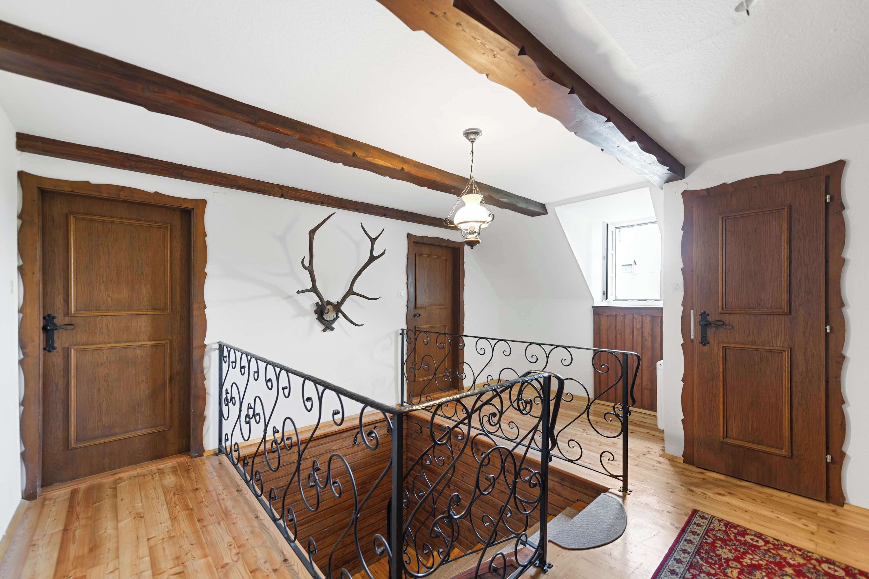 A wooden staircase with ornate metal railings, wooden doors, and a ceiling with exposed beams.