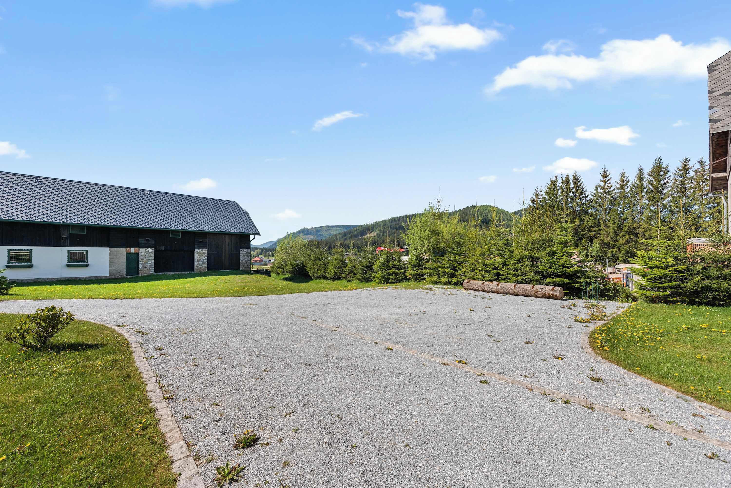 A building with a sloped roof and a gravel driveway leading to a grassy area.