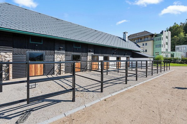 A stable with a metal fence, stone walls, and a green roof.