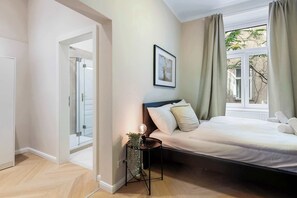 A bedroom with a bed, a bedside table with a lamp, a window with curtains, and a door leading to another room. - Kaiser 1BR | Metro & Tram | Nespresso | Central (Wien)