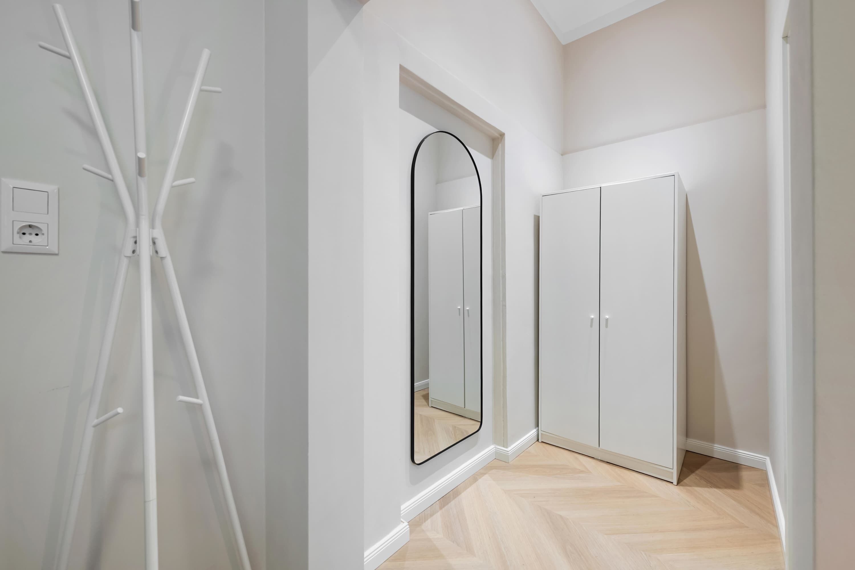 A hallway with a white wardrobe, a mirror, and a white radiator.