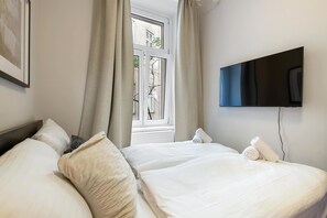 A hotel room with a bed, a TV mounted on the wall, and a window with curtains. - Kaiser 1BR | Metro & Tram | Nespresso | Central (Wien)