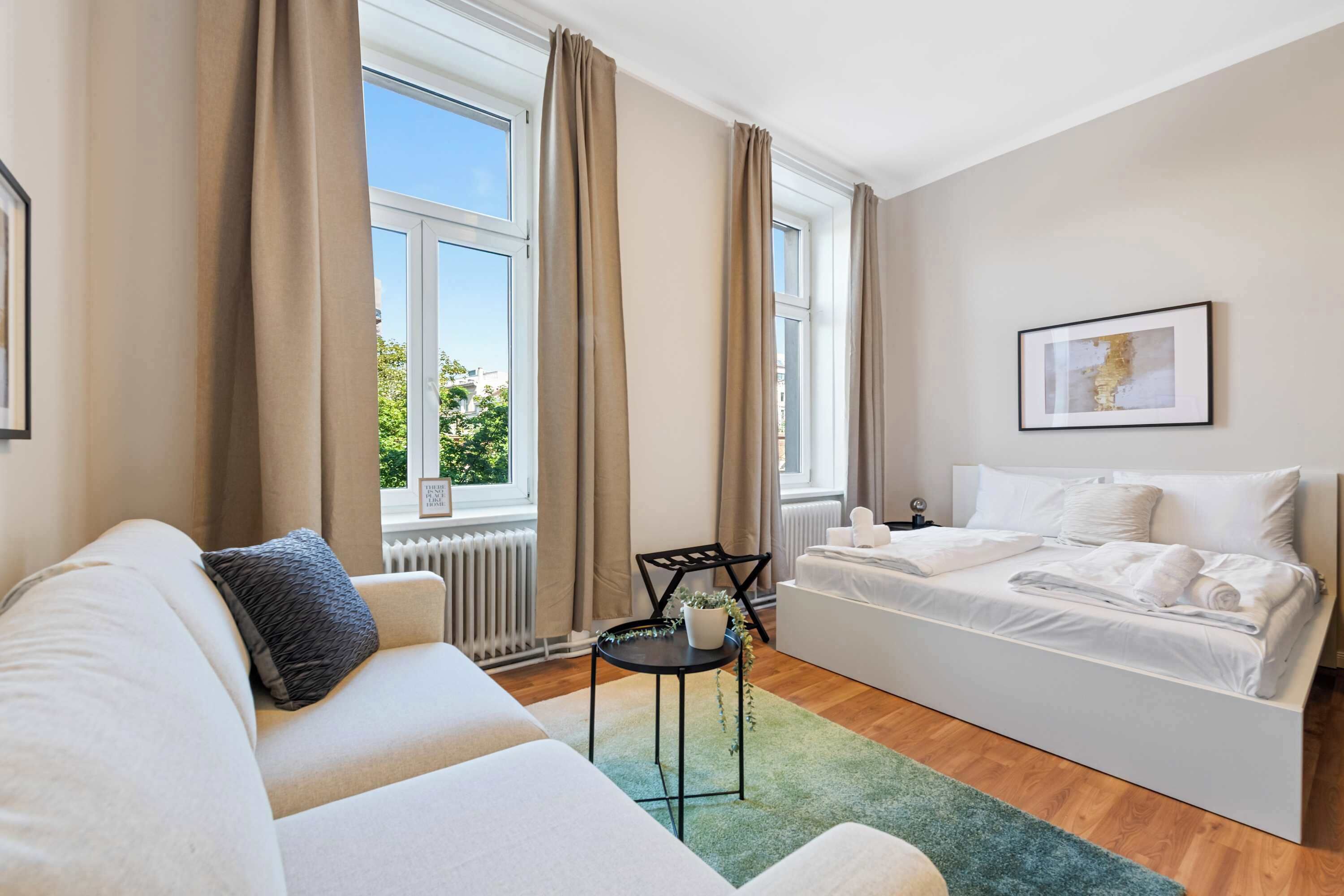 Une chambre d’hôtel moderne, équipée d’un lit, d’un canapé, d’une petite table et d’une fenêtre avec des rideaux.
