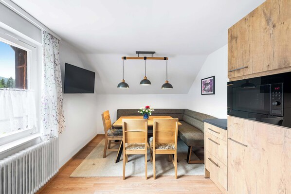 A modern kitchen with wooden cabinets, a dining table with chairs, pendant lights, and a large window with curtains.