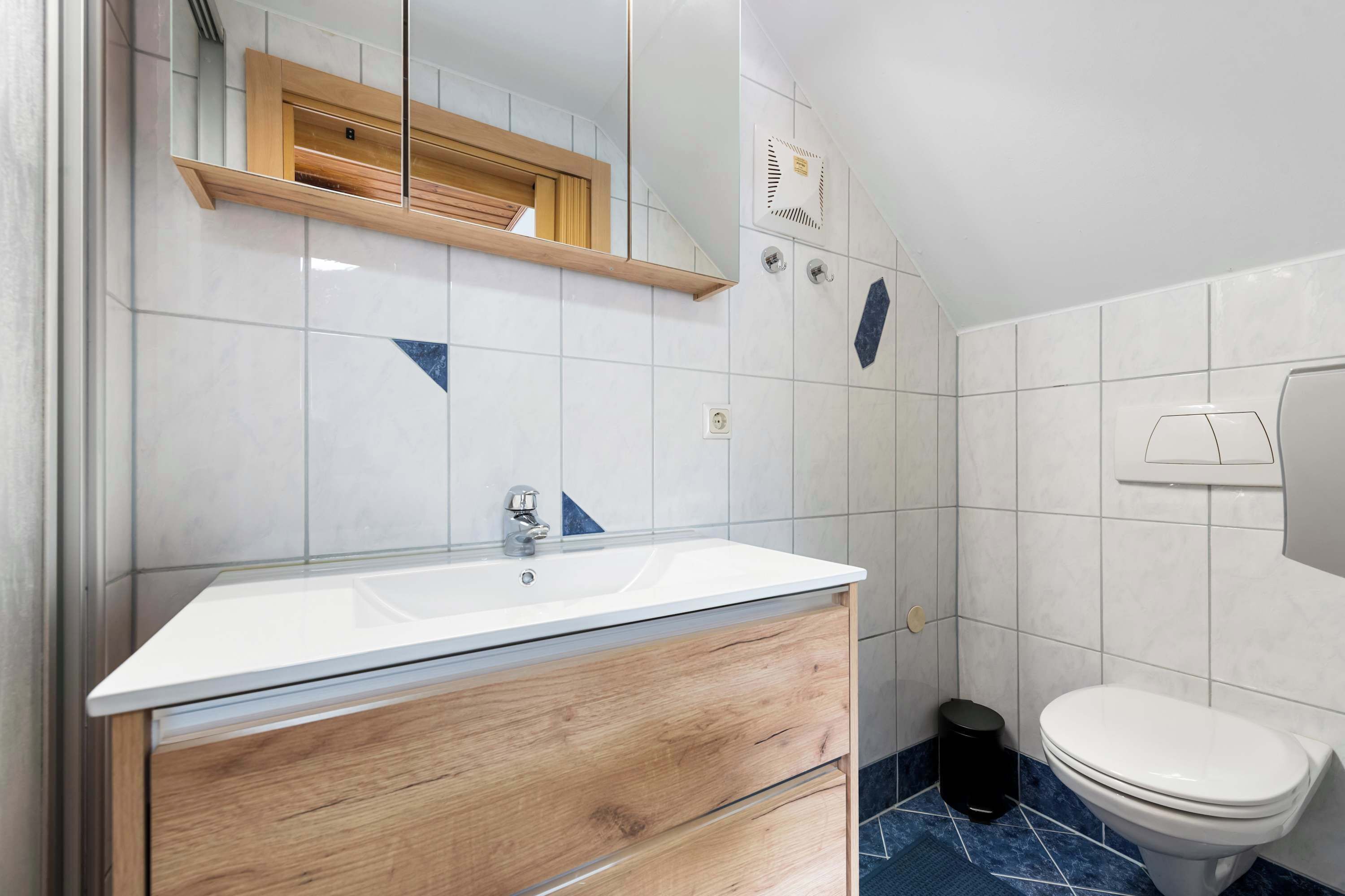 Un bagno con lavandino bianco, mobile contenitore in legno, specchio e water.