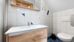 A bathroom with a white sink, wooden vanity, a mirror, and a toilet.