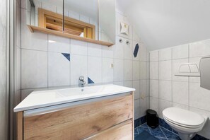 Un bagno con lavandino bianco, mobile contenitore in legno, specchio e water.