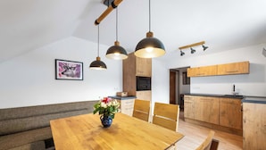 A modern kitchen with wooden cabinets, a dining table with chairs, and pendant lighting.