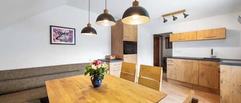 Une cuisine moderne avec des meubles en bois, une table à manger avec des chaises et des luminaires suspendus.