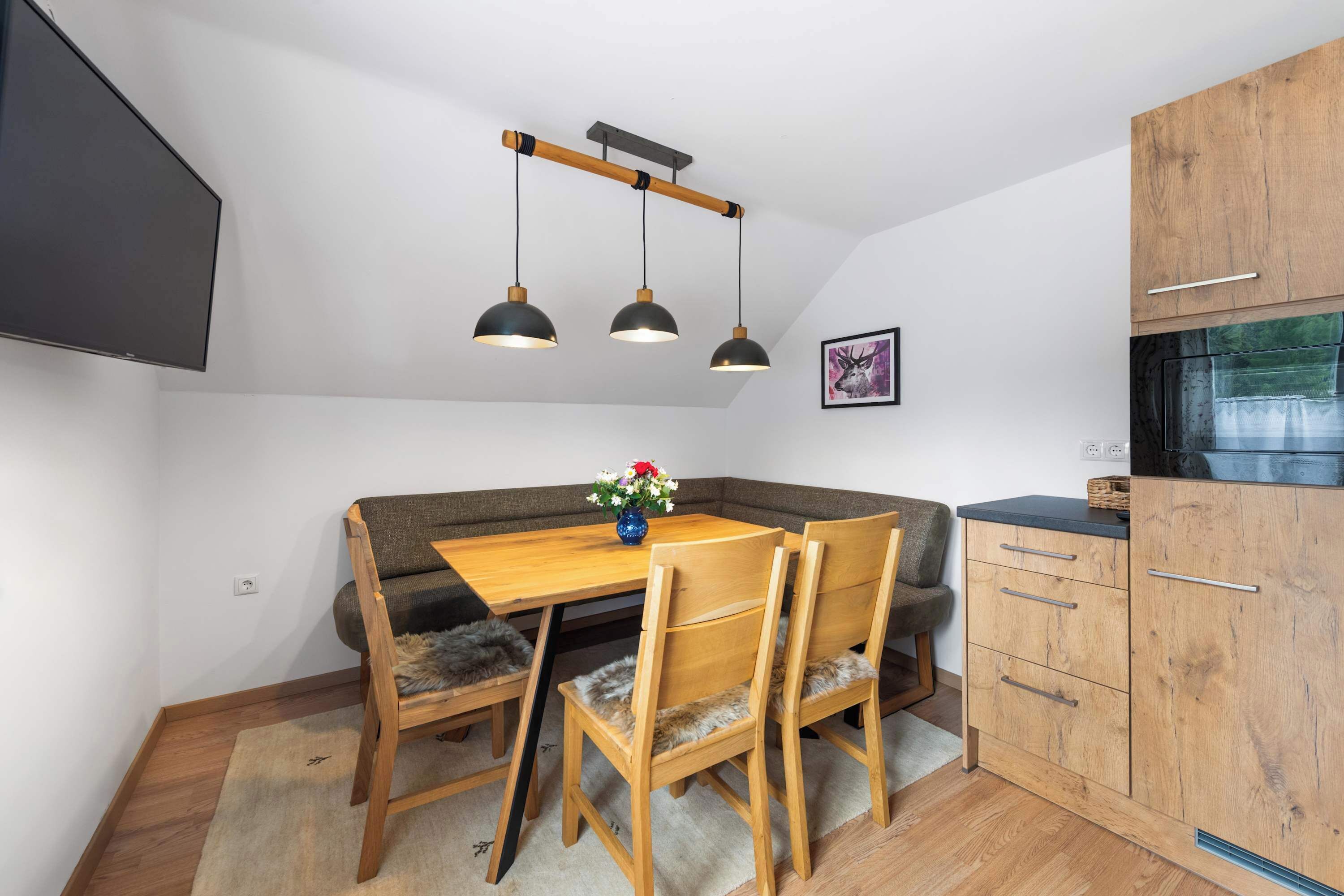 A compact kitchen with a dining area, wooden cabinets, and a modern pendant light fixture.